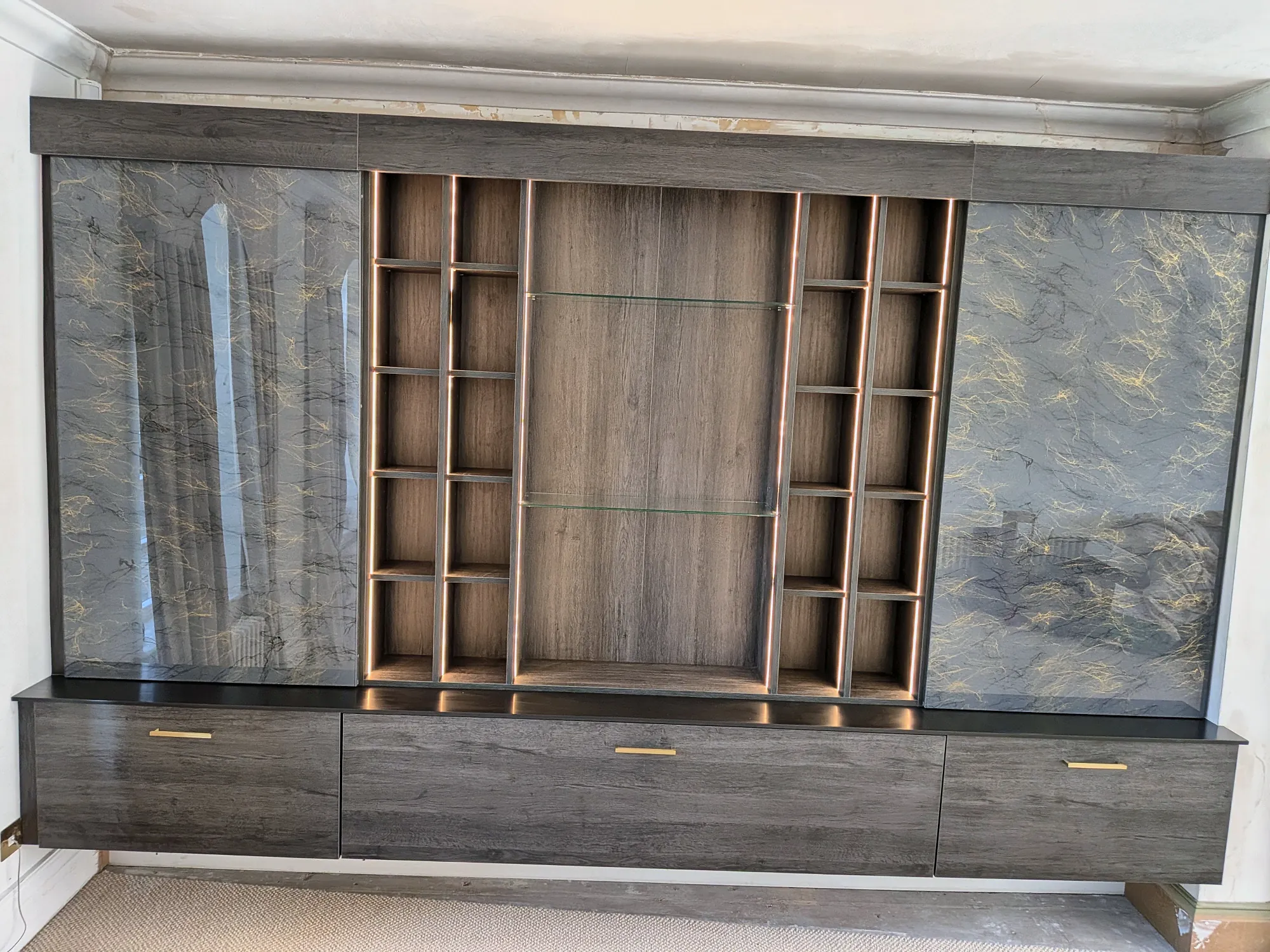 Dark oak media wall with marble-effect panels and lit open shelving
