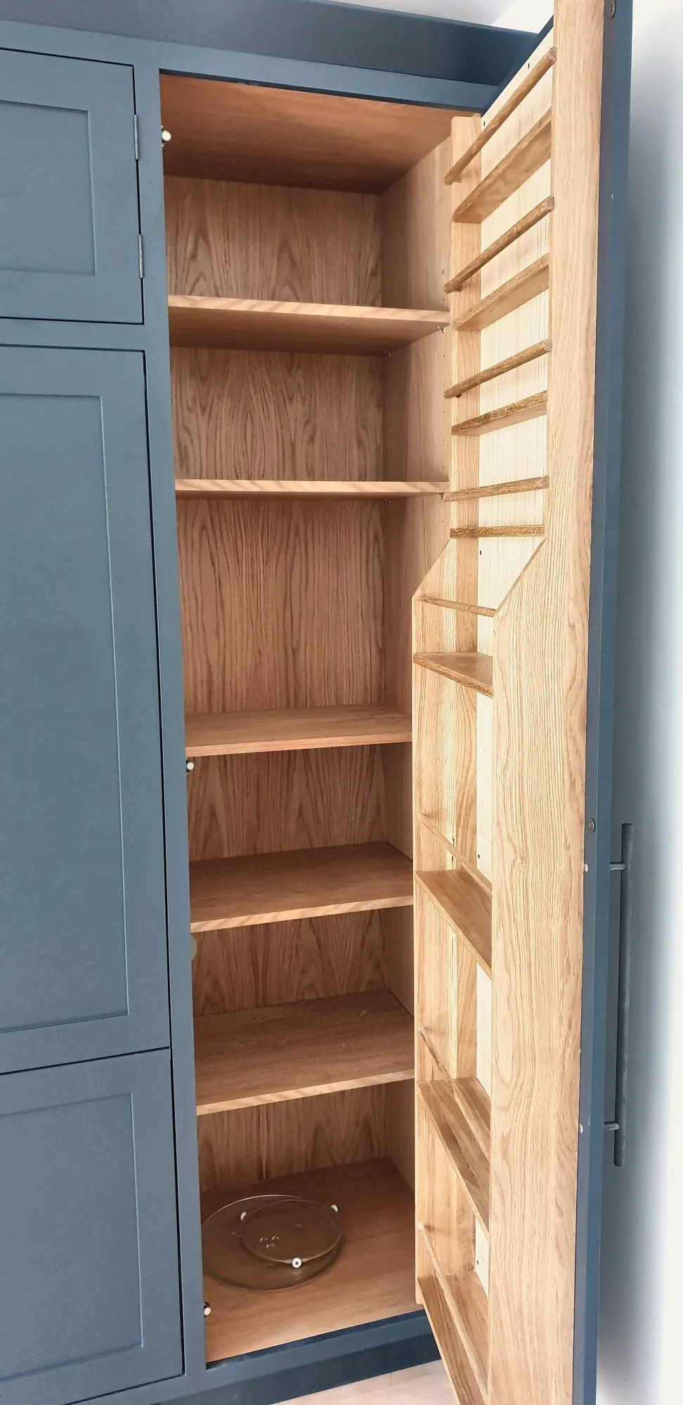 Oak larder shelving behind a navy door